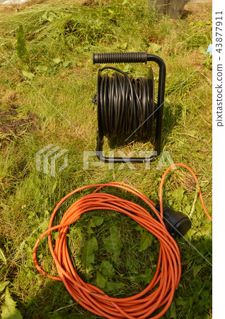 Coil with electric cable and extension cord on the grass, electric tools for construction works in Coil with electric cable and extension cord on the grass, electric tools for construction works in 43877911