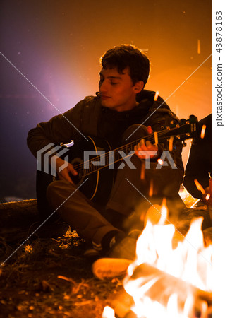 guy playing guitar around a campfire on the guy playing guitar around a campfire on the 43878163