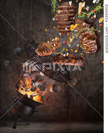Kettle grill with hot briquettes, cast iron grate and tasty beef steaks flying in the air. 43884008