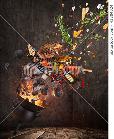 Kettle grill with hot briquettes, cast iron grate and tasty beef steaks flying in the air. 43884024