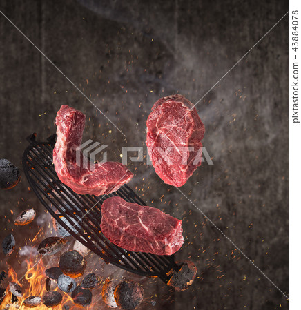 Kettle grill with hot briquettes, cast iron grate and tasty beef steaks flying in the air. 43884078