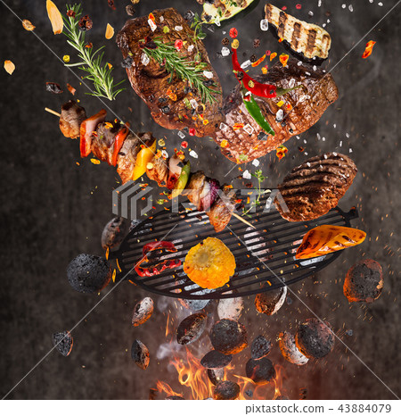 Kettle grill with hot briquettes, cast iron grate and tasty meats flying in the air. 43884079