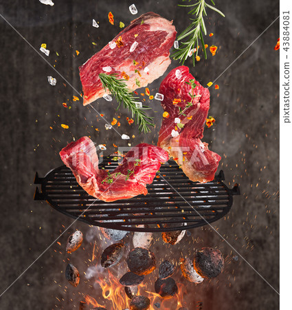 Kettle grill with hot briquettes, cast iron grate and tasty beef steaks flying in the air. 43884081