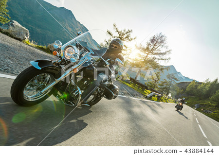 Motorcycle driver riding japanese high power cruiser in Alpine highway on famous Hochalpenstrasse, Austria. Motorcycle driver riding japanese high power cruiser in Alpine highway on famous Hochalpenstrasse, Austria. 43884144