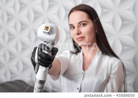 A female cosmetologist holds a device for laser hair removal. On the background of a modern beauty A female cosmetologist holds a device for laser hair removal. On the background of a modern beauty 43889850