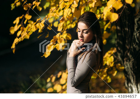 Young and pretty brunette girl in a dress and scarf stands near a beautiful big yellow tree 43894657