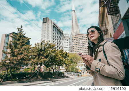 woman searching by phone standing in street woman searching by phone standing in street 43916190