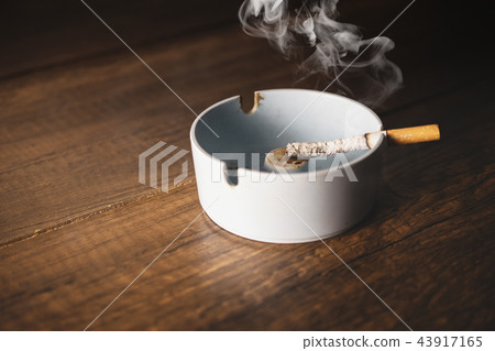 ashtray with cigarette on wood table. 43917165