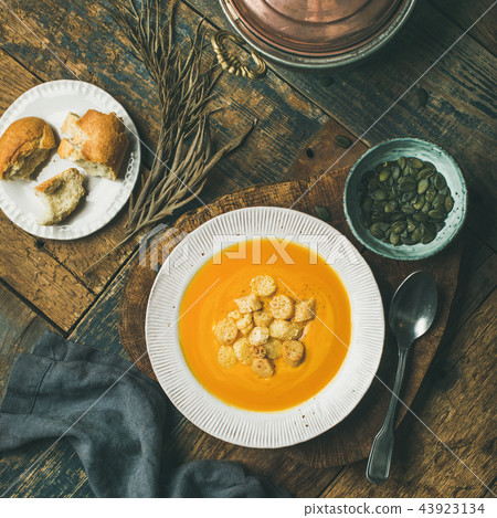 Warming pumpkin cream soup with croutons and seeds on board 43923134