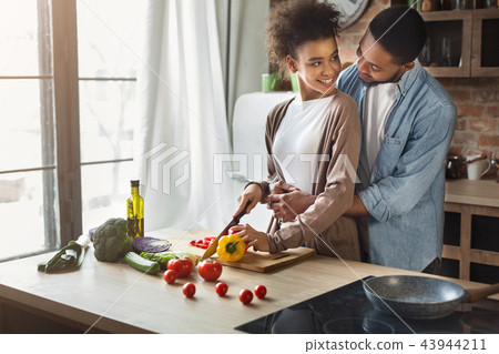 Loving black husband hugging wife while cooking Loving black husband hugging wife while cooking 43944211