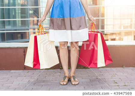 Consumerism, sale and people concept - Close up of woman carrying shopping bags while walking along 43947569
