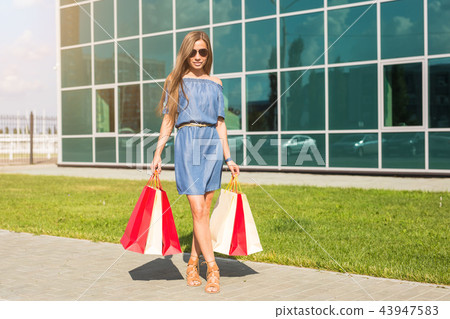 Purchase, discount and people concept - portrait of young woman in dress walking with colorful 43947583