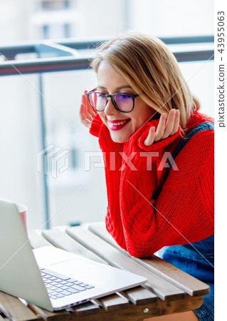 girl in red sweater sitting at table with computer girl in red sweater sitting at table with computer 43955063