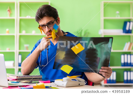 Young doctor sitting in hospital with many conflicting prioritie Young doctor sitting in hospital with many conflicting prioritie 43958189