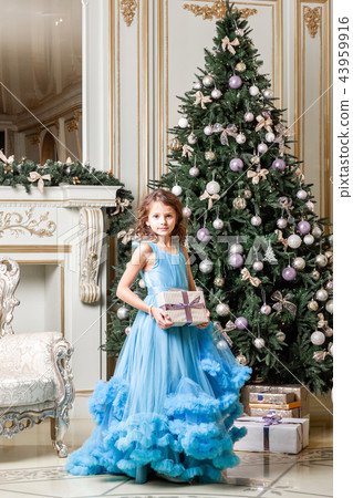 Beautiful little girl sitting near to a Christmas tree. Charming daughter in blue dress. New year Beautiful little girl sitting near to a Christmas tree. Charming daughter in blue dress. New year 43959916