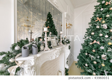 White fireplace decorated with candles and fir branches. Decorated Christmas tree. Classic 43960031