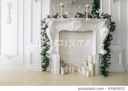 White fireplace decorated with candles and fir branches. Decorated Christmas tree. Classic White fireplace decorated with candles and fir branches. Decorated Christmas tree. Classic 43960032