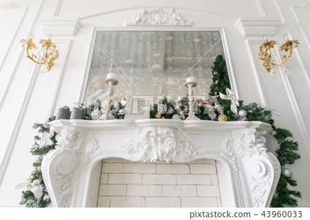 White fireplace decorated with candles and fir branches. Decorated Christmas tree. Classic White fireplace decorated with candles and fir branches. Decorated Christmas tree. Classic 43960033
