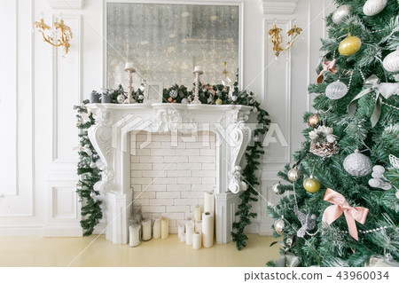 White fireplace decorated with candles and fir branches. Decorated Christmas tree. Classic White fireplace decorated with candles and fir branches. Decorated Christmas tree. Classic 43960034