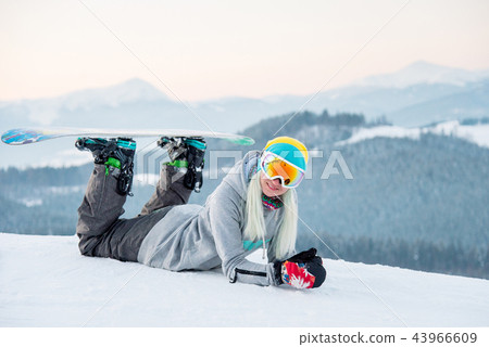 Young woman snowboarder relaxing outdoors lying on the snow smiling to the camera joyfully 43966609