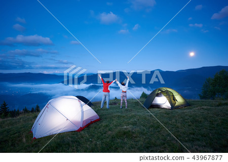 Rear view good friends near camping in mountains holding hands raised them upwards Rear view good friends near camping in mountains holding hands raised them upwards 43967877