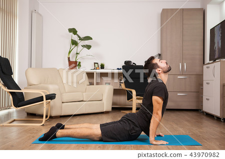 Young adult doing cobra yoga pose on his house floor Young adult doing cobra yoga pose on his house floor 43970982