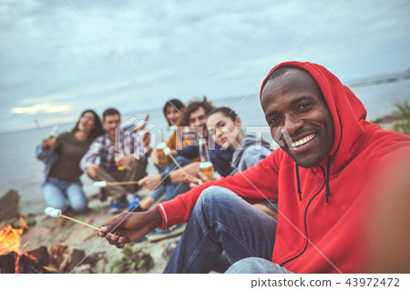 Guy frying marshmallows with his friends at the beach 43972472