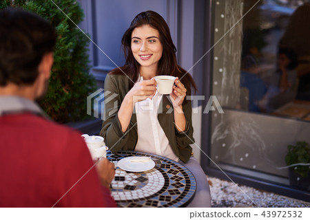 Charming young lady enjoying meeting with friend in outdoor cafe Charming young lady enjoying meeting with friend in outdoor cafe 43972532