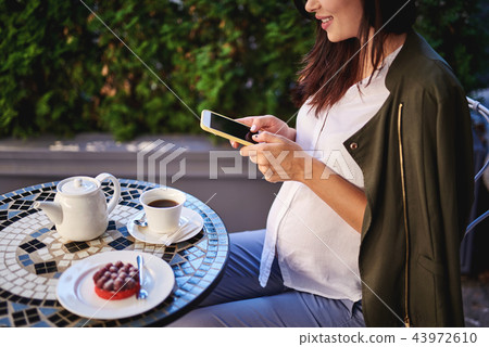Lovely pregnant lady using cellphone in outdoor cafe Lovely pregnant lady using cellphone in outdoor cafe 43972610