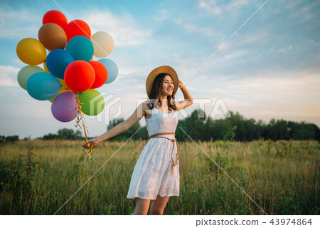 Smiling woman with balloons walking in green field Smiling woman with balloons walking in green field 43974864