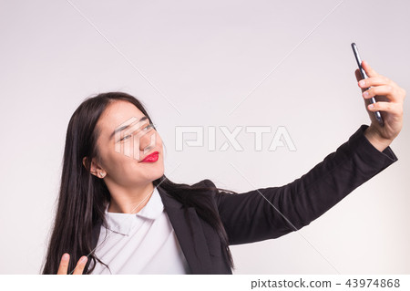 Technology, smartphone and people concept - Happy young asian woman making selfie over white 43974868