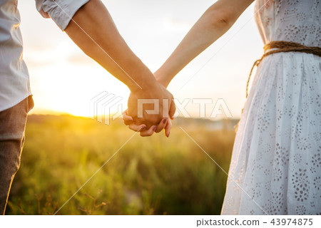Couple hold hands in green field on sunset Couple hold hands in green field on sunset 43974875