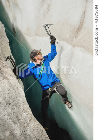 A free climber without insurance with two ice axes rises from a crack in the glacier. Free climbing A free climber without insurance with two ice axes rises from a crack in the glacier. Free climbing 43975694