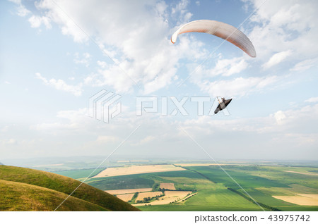 A white-orange paraglider flies over the mountainous terrain A white-orange paraglider flies over the mountainous terrain 43975742