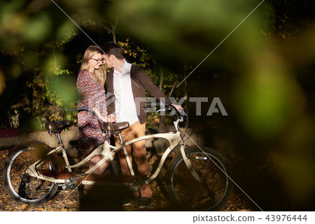 Romantic couple, man and attractive girl close together at tandem bicycle in dark autumn park. 43976444