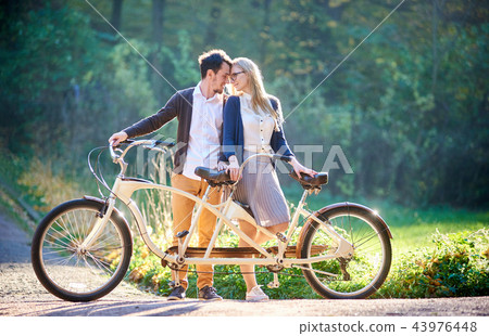 Young couple, handsome man and attractive woman on tandem bike in sunny summer park or forest. 43976448