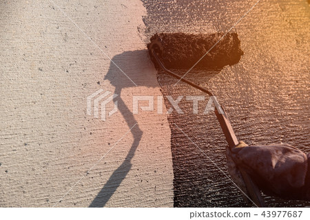 Roofer worker painting black coal tar or bitumen at concrete 43977687