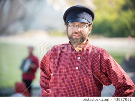 A man in a Russian-folk costume stands on a background of water and poses for the camera A man in a Russian-folk costume stands on a background of water and poses for the camera 43987931