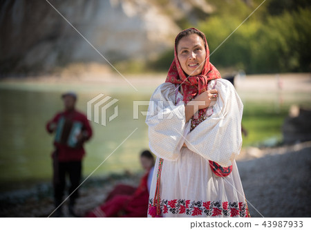 A woman in Russian folk clothes with a beautiful ornament, the sun is shining A woman in Russian folk clothes with a beautiful ornament, the sun is shining 43987933