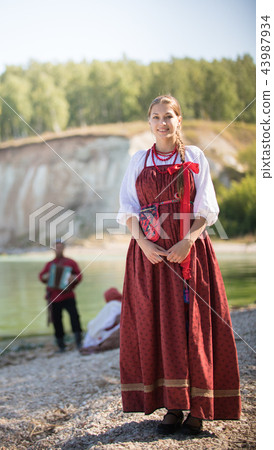 Portreat of a young woman in a Russian folk costume stands on the background of a wonderful 43987934