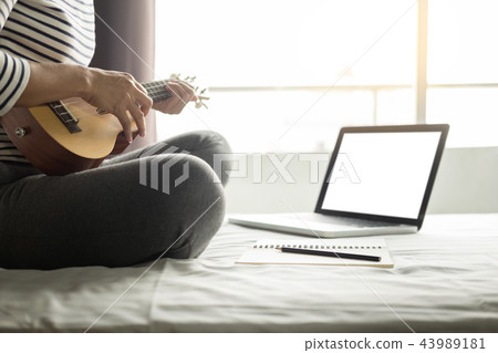Happy young asian woman playing ukulele sitting on bed in bedroo Happy young asian woman playing ukulele sitting on bed in bedroo 43989181