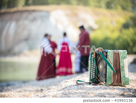 Shot of the accordion, on the background of a group of young people in Russian national red costumes Shot of the accordion, on the background of a group of young people in Russian national red costumes 43993136