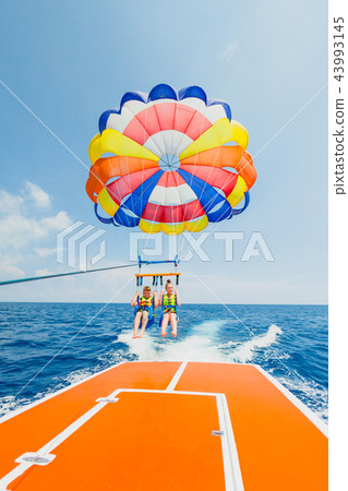 Couple of tourists flying on a multi colored parachute 43993145