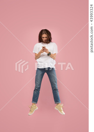 Full length of pretty young woman with mobile phone while jumping 43993324