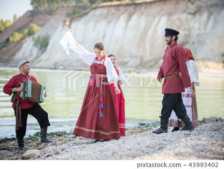 Beautiful young people in Russian national costumes dancing, playing accordion 43993402