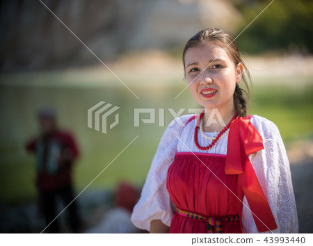 A girl in red Russian national costume stand on the background of an amazing landscape close up shot A girl in red Russian national costume stand on the background of an amazing landscape close up shot 43993440