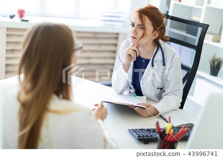 A beautiful young girl in a white robe is sitting at the desk in the office and communicating with A beautiful young girl in a white robe is sitting at the desk in the office and communicating with 43996741