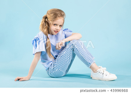 A girl in blue clothes is sitting on a blue background. A girl in blue clothes is sitting on a blue background. 43996988