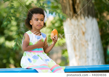 A black girl is sitting on a bench with bread. 44004698