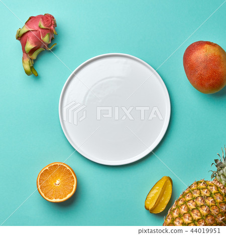 Different tropical fruits and empty white plate on a blue background with copy space. Flat lay Different tropical fruits and empty white plate on a blue background with copy space. Flat lay 44019951